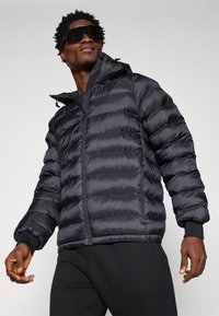 Giubbotto imbottito nero con chiusura a zip, cappuccio e polsini elasticizzati. Il tessuto è liscio e lucido, con una texture trapuntata.
