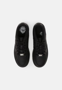 Svarta sneakers med slät läderöverdel, perforerad tåbox, platta snören och en silverdetalj på tungan. Strukturerad gummisula.