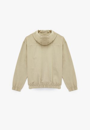 Beige capuchonjack met een ontspannen pasvorm, elastische tailleband en boorden. Het heeft een zachte textuur en een eenvoudig, strak ontwerp.