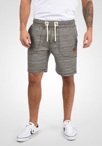 Shorts en tricot gris avec une taille à cordon, deux poches avant et un tissu texturé. Présente un petit patch logo marron sur le côté.