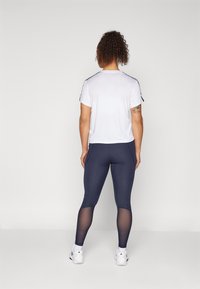 Maglietta atletica bianca a maniche corte con dettagli neri sulle spalle, abbinata a leggings blu navy con pannelli in rete. Sneakers bianche completano l'outfit.