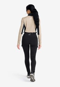 Kompressionslinne med lång ärm i ljusbrun och svart, kombinerat med högmidjade svarta leggings med sidofickor och texturerade paneler.