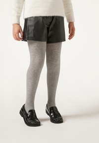 Svarta fusk läder shorts kombinerat med gråa strumpbyxor och svarta loafers. Shorts har en slät yta, medan strumpbyxorna är stickade och mjuka.