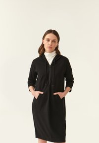 Robe hoodie noire avec une poche kangourou, des manches longues et une capuche à cordon de serrage. Fabriquée dans un matériau doux avec une texture lisse.