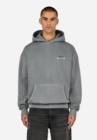 Sivá bavlnená mikina s kapucňou, ktorá obsahuje klokanie vrecko, rebrované manžety a malé modré logo "Sport Club" na hrudi. Voľný strih.