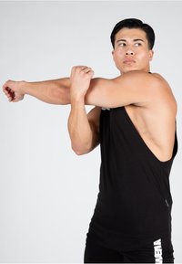 Melna bezpiedurkņu tanka ar atvērtu aizmuguri. Audums šķiet mīksts. Modele stiepjas uz neitrāla fona.