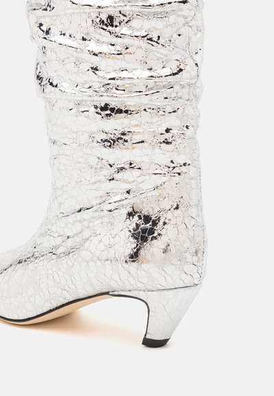 Silberne kniehohe Stiefel mit geriffeltem Lack-Finish, konischem Absatz und einer strukturierten Oberfläche mit einem rissigen Muster.