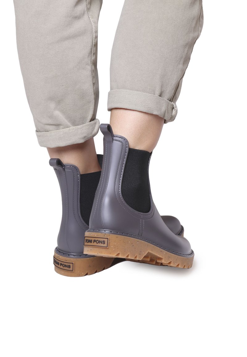 Botas Chelsea de goma grises con paneles elásticos laterales negros y suelas marrones texturizadas. Marca en el tacón. Pantalones enrollados de color beige claro.