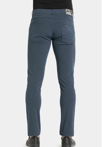 Jeans in cotone blu scuro, slim-fit, con due tasche posteriori e un piccolo etichetta del marchio sulla vita. Texture liscia e dettagli minimi.