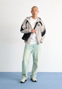 Light gray windbreaker with black accents, white t-shirt, light blue jeans, and beige sneakers. Black crossbody bag worn on left side.