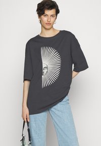 Tmavě šedé oversized tričko s grafickým motivem slunce a měsíce a vyzařujícími bílými liniemi. Měkký bavlněný materiál, uvolněný střih, krátké rukávy.