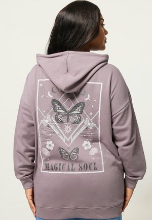 Frau mit einem maulbeerfarbenen Hoodie, auf dessen Rückseite Schmetterlings-, Blumen- und Mondphasenmotive sowie der Schriftzug "MAGICAL SOUL" zu sehen sind, von hinten betrachtet.