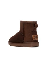 Bota de tobillo de ante marrón con puntera redonda, superficie texturizada y un tab lateral reforzado. Presenta un parche de logo en color marrón claro en el lado exterior.