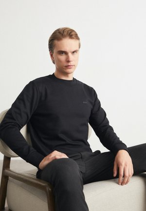 Black long-sleeve sweatshirt with a round neckline, made of cotton, features subtle "BOSS" logo on the chest, paired with black trousers.