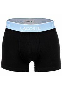 Boxer da uomo neri con vita azzurro chiaro che presenta la scritta "LACOSTE" in bianco e un piccolo logo di coccodrillo verde sull'etichetta interna.