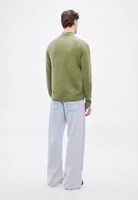 Zöld kötött pulóver magas gallérral, világoskék bőszárú farmerrel párosítva. A szövet puha tapintású és minimális varrás van rajta.