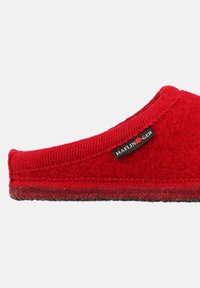 Pantofole di feltro rosse con punta arrotondata, suola piatta e bordature testurizzate. Presenta un'etichetta nera con il logo "Haflinger" sul lato.