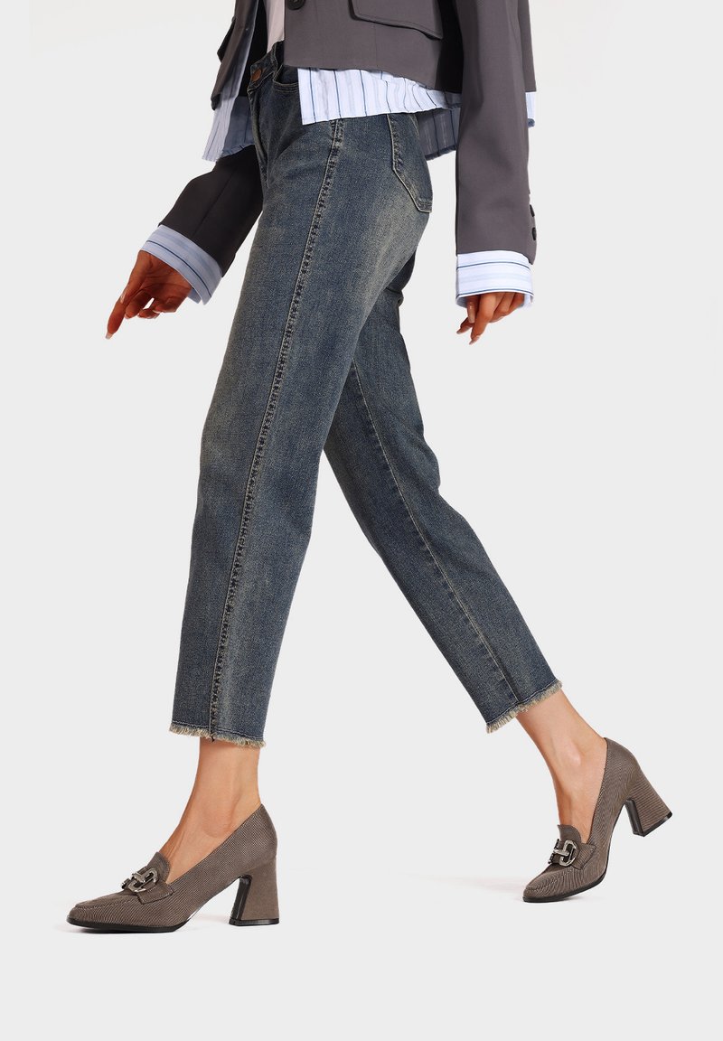 Scarpe con tacco in pelle marrone con punta quadrata, tacco medio a blocco e dettaglio decorativo a fibbia, abbinate a jeans cropped in denim chiaro.