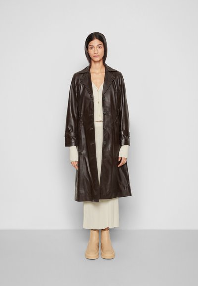 Mantem de pele castanha com colarinho de lapela, fecho de botões e bolsos laterais. Combinado com um vestido creme canelado e botas de plataforma bege.