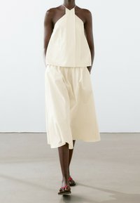 Haut halter beige clair associé à une jupe midi fluide assortie. Design simple avec une texture lisse et une coupe décontractée. Porté avec des sandales plates.