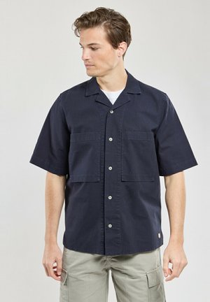 Chemise en navy à manches courtes avec col camp, dotée de deux poches à l'avant et d'une fermeture à boutons. Fabriquée en coton avec une texture lisse.