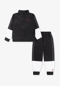 Black tracksuit with zippered jacket and elastic waist pants. Features white panel accents and red logo on chest and leg. Smooth texture.