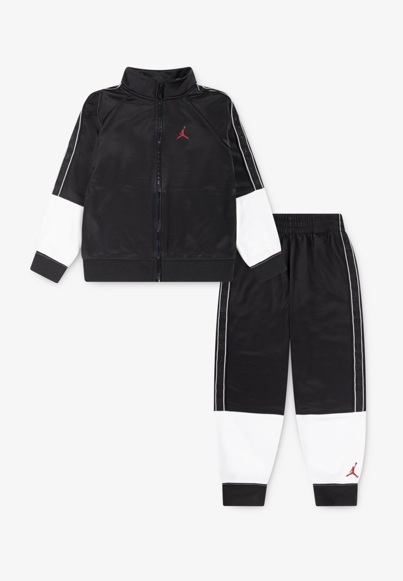 Black tracksuit with zippered jacket and elastic waist pants. Features white panel accents and red logo on chest and leg. Smooth texture.