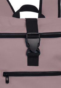 Mochila púrpura con un acabado suave, que presenta un cierre de cremallera negro, cierre de hebilla y correas ajustables. Diseño simple con bolsillos de doble cremallera.