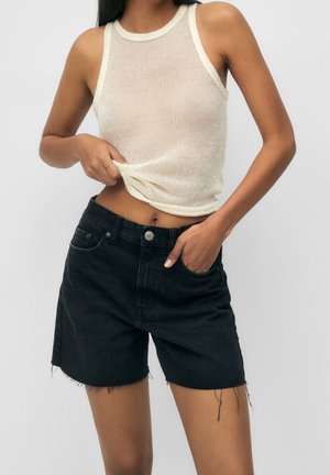 Black denim shorts with a frayed hem and pockets, paired with a light beige, sheer, sleeveless top featuring a ribbed texture.