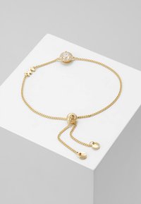 Pulsera de cadena de oro con una piedra redonda clara central rodeada de piedras más pequeñas, con cierre ajustable y charms decorativos en los extremos.