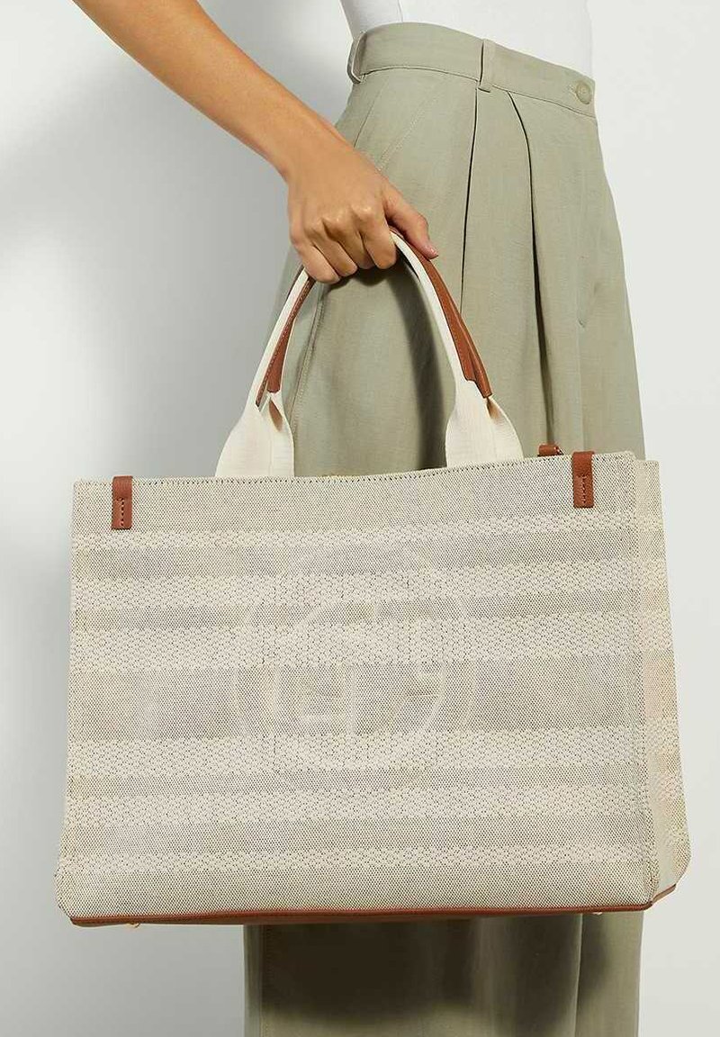 Sac fourre-tout tissé beige avec des rayures horizontales, des accents marron et deux poignées. Surface texturée et détail de marque à l'avant.