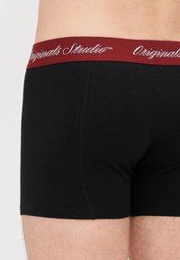 Boxers en coton noir avec une taille élastique bordeaux arborant la marque "Originals Studio" en blanc, texture lisse et design ajusté.