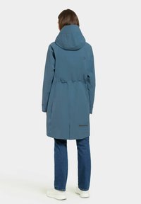 Veste en teal résistante à l'eau avec une grande capuche, une taille cintrée et des poches latérales ; présente un accent noir près de l'ourlet.
