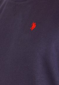 Marineblauw stof met een klein rood geborduurd logo van een polo speler te paard dicht bij het borstgebied.