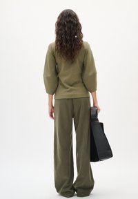 Olivgrünes, lässiges Oberteil mit Dreiviertelärmeln, kombiniert mit passenden weit geschnittenen Hosen; schwarze Tasche mit Griff.