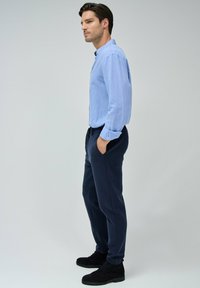 Camisa abotonada de color azul claro con mangas largas, combinada con unos pantalones de cintura elástica en navy y botines de ante negros. Textura suave y diseño ajustado.