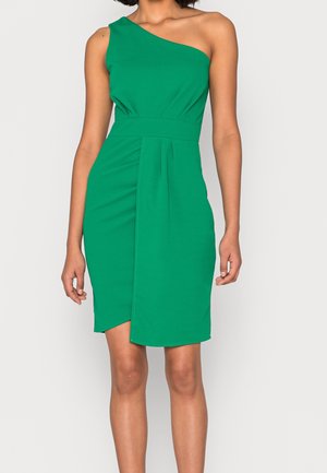 Femme portant une robe verte sans manches, à une épaule, longueur au genou, avec une taille cintrée et un pli sur le devant.