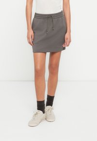 Φούστα από γκρι βαμβακερό μείγμα με ελαστική μέση και κορδόνι. Διαθέτει απλό σχέδιο και ριμπ τελείωμα. Φορεμένη με μπεζ αθλητικά παπούτσια.