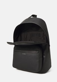 Zaino nero realizzato in materiale sintetico liscio. Dotato di un compartimento principale con zip e una tasca frontale, con il logo Calvin Klein sulla parte anteriore.