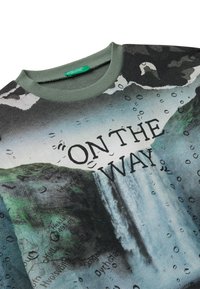 Mikina se zeleným žebrovaným límcem, potiskem vodopádu a mapy, kapkami vody a textem "NA CESTĚ" velkými černými písmeny.