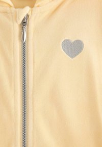 Gul fleece zip-up sweatshirt med et sølv hjertepatch, en frontlynlås og en blød tekstur.