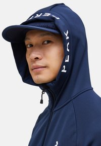 Chaqueta con capucha de color azul marino, con cremallera y detalles de logo. Presenta un diseño ajustado y una capucha estilo gorra con una textura suave.