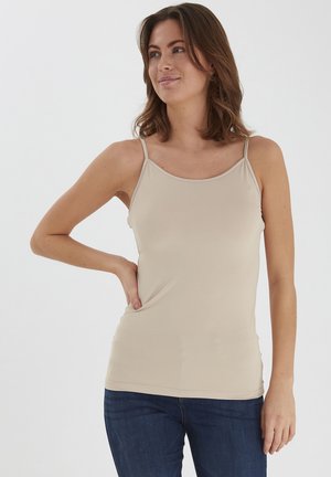 Beige Tanktop mit dünnen Trägern, figurbetontem Design, glatter Textur und geradem Saum. Getragen mit dunkelblauen Jeans.