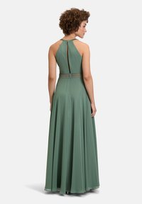 D długa, bezrękawnikowa zielona sukienka z dekoltem halter, odkrytą plecami i ozdobnym pasem. Gładka faktura i długość do podłogi.