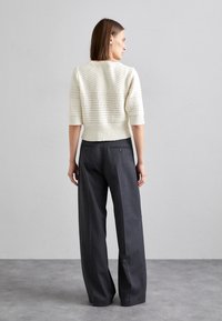 Cremfarbener gestrickter Pullover mit kurzen Ärmeln und strukturiertem Design, kombiniert mit hoch taillierten, dunkelgrauen weit geschnittenen Hosen.