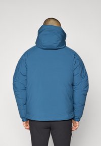 Blå puffjacka med huva, med en slät textur, elastiska ärmavslut och en avslappnad passform. Synlig sömnad och inga ytterligare detaljer.