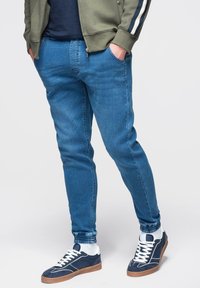 Jeans di denim blu a taglio slim, con una texture liscia. Abbinati a sneakers blu navy e bianche, dal design sportivo.