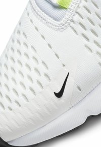 White athletic shoe with a breathable mesh upper, textured detailing, a black logo, and a vibrant yellow accent on the tongue.