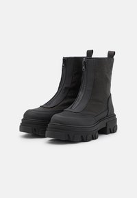 Botas negras hasta el tobillo con un upper de nylon texturizado, doble cremallera y suelas de goma gruesas. Presentan puntera reforzada y lengüetas para un fácil calce.
