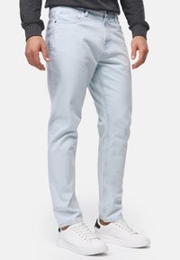 Jeans in denim azzurro chiaro con vestibilità slim, caratterizzati da leggere sfumature, cinque tasche e abbinati a sneakers bianche.
